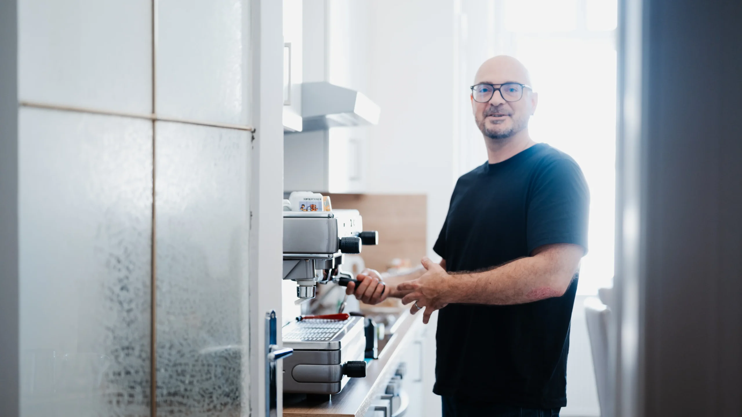 Mitarbeiter steht willkommen heißend an der Kaffeemaschine und bereitet Kaffee zu