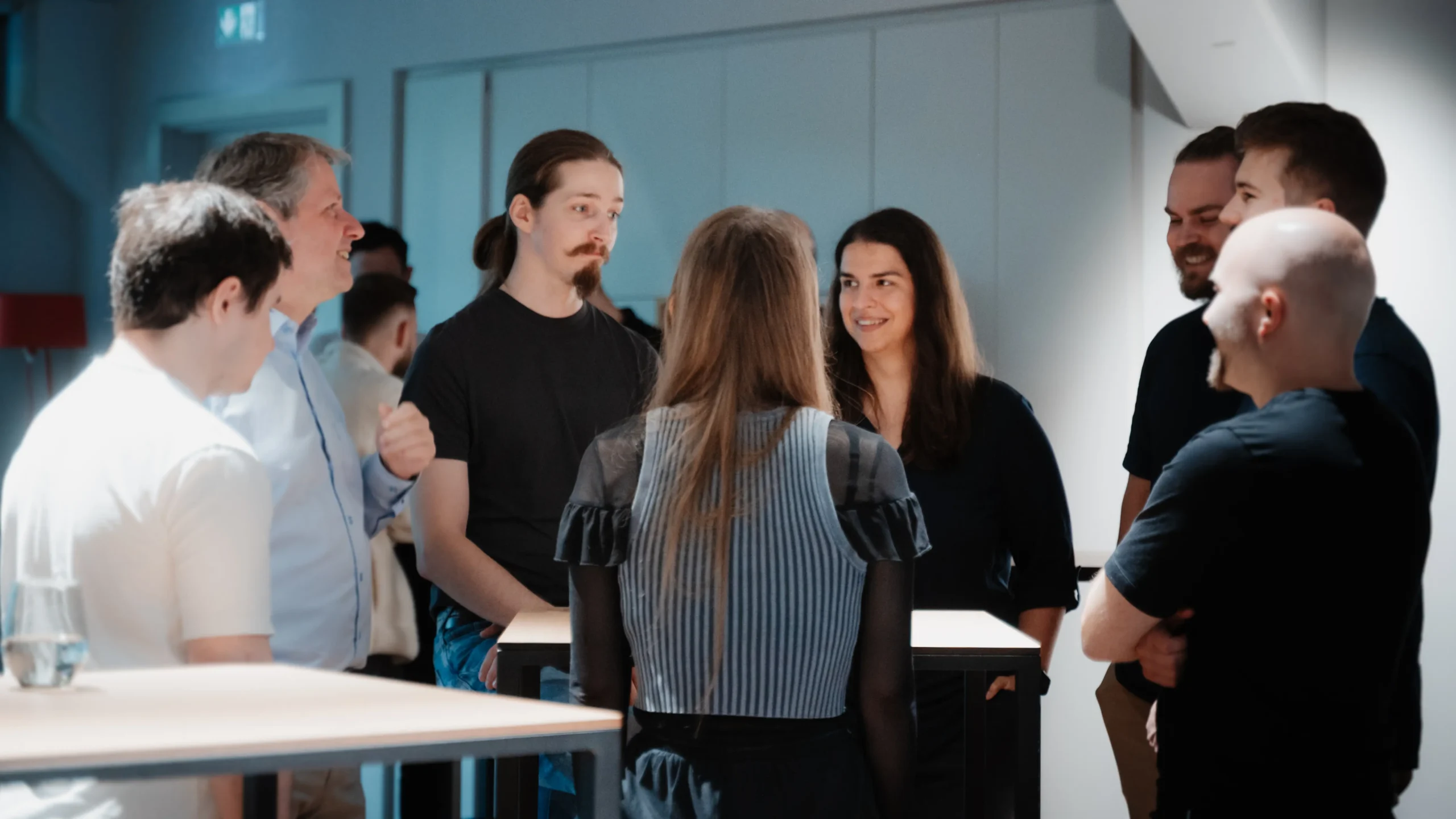 Mitarbeiterinnen und Mitarbeiter stehen im Kreis um einen Tisch und tauschen sich freudig aus