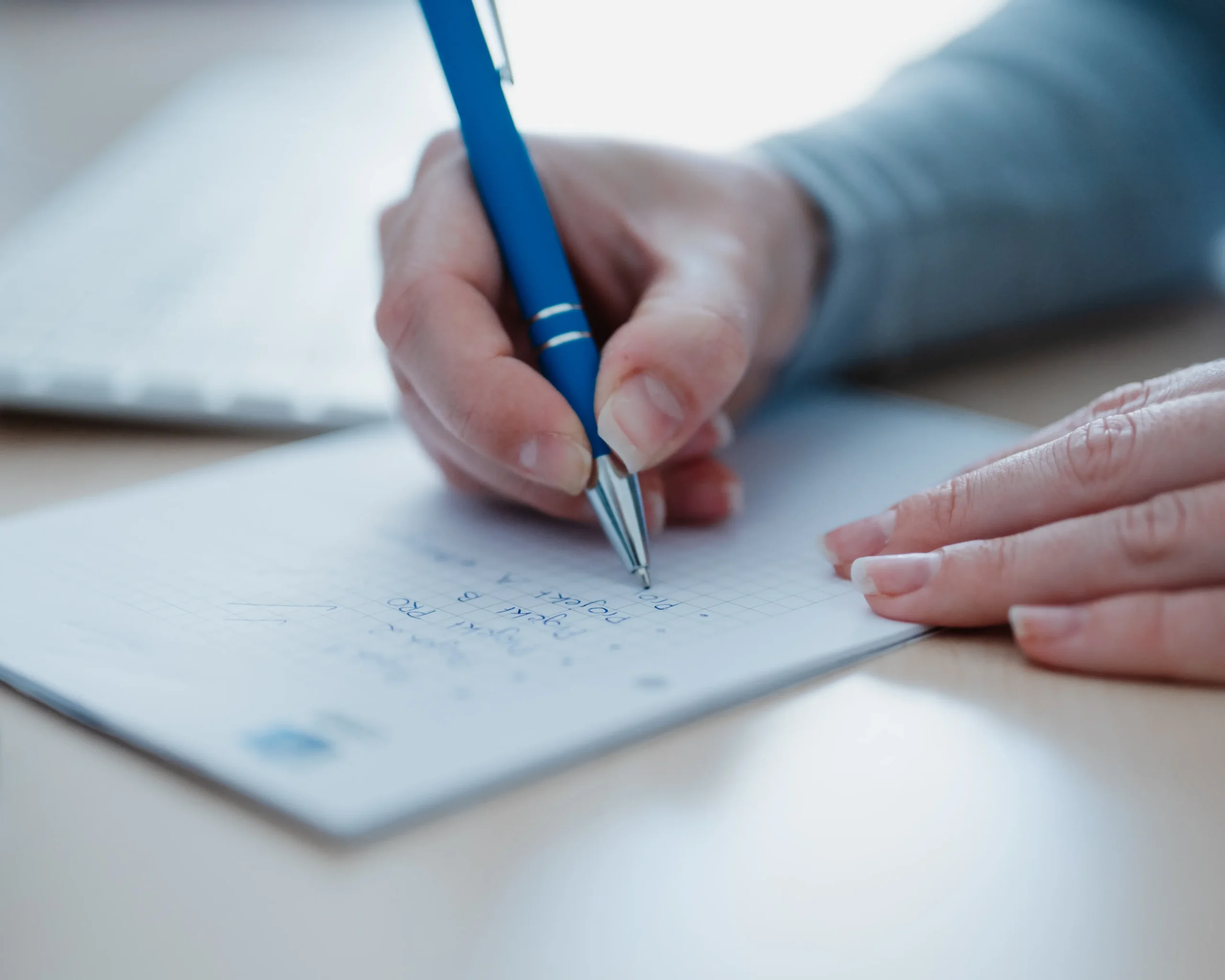 Hände machen mit einem Kugelschreiber Notizen auf einem Notizblock