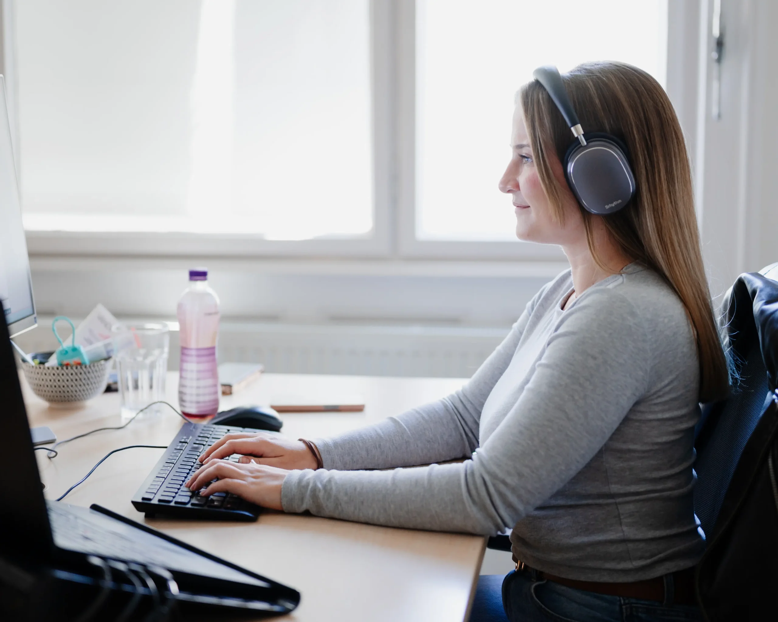 Eine Mitarbeiterin der Datenmanagement Abteilung arbeitet mit Kopfhörern vor mehreren Computerbildschirmen