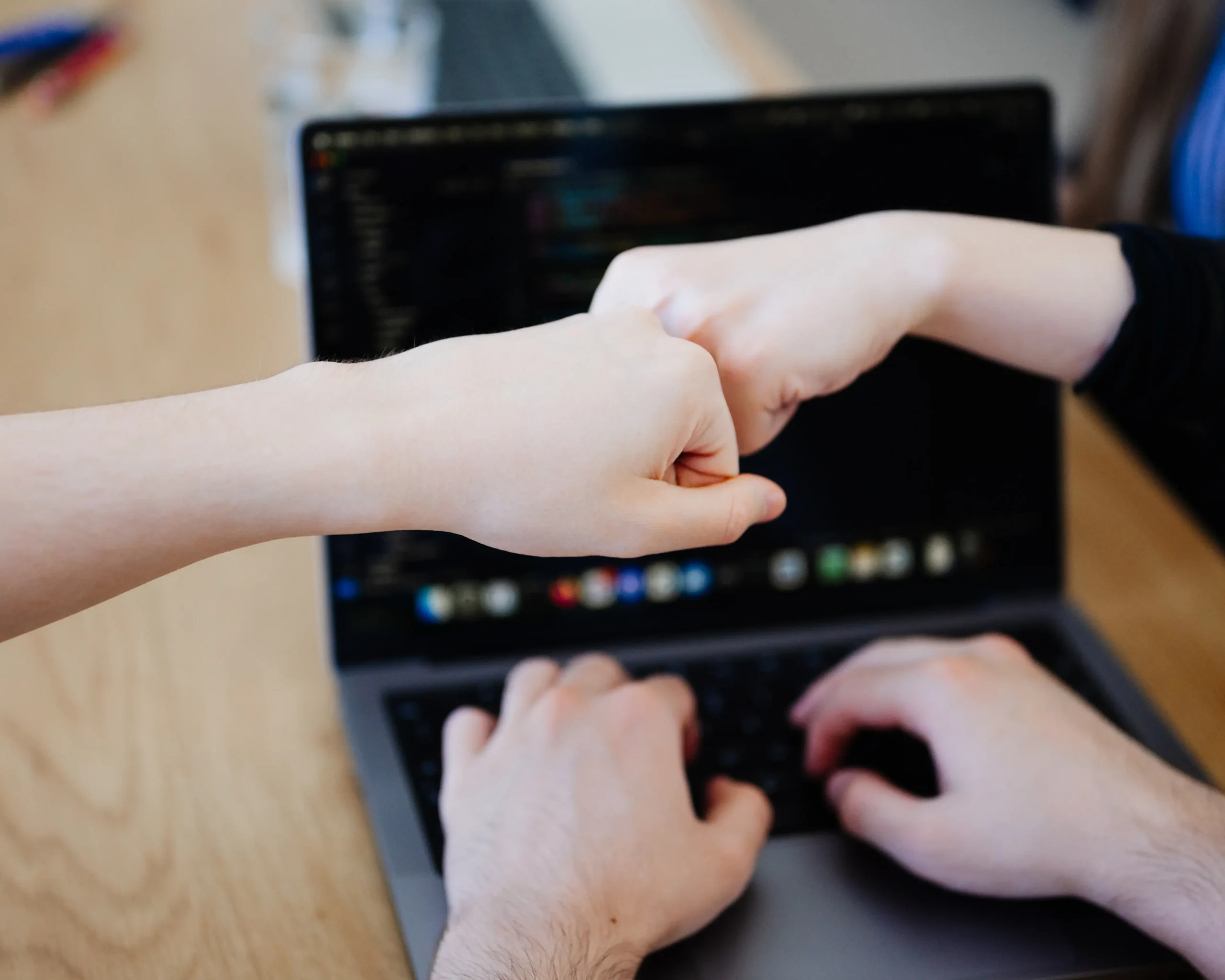 Eine Mitarbeiterin und ein Mitarbeiter geben sich bei der Zusammenarbeit an einem Projekt über einem Laptop die Faust, während ein weiterer Kollege tippt